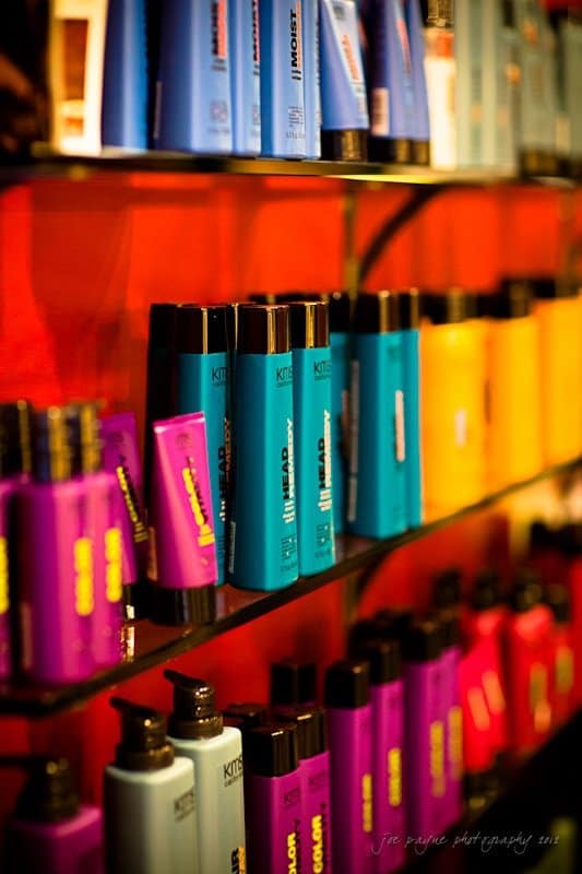 Shelves filled with colorful haircare products in various brightly colored bottles, including blue, purple, and yellow, neatly arranged against a red background.