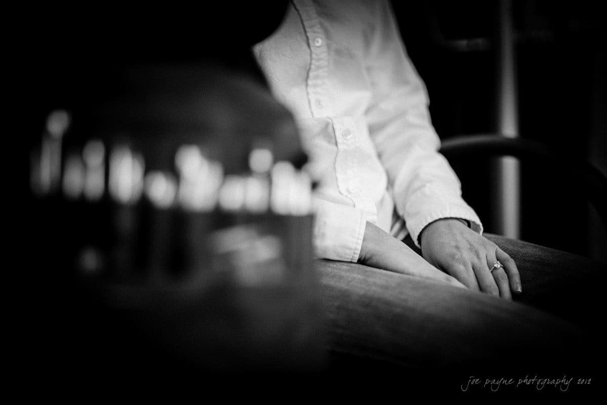A person in a white shirt and jeans is sitting with their right hand resting on their knee. The focus is on their hand, which has a ring. The background is blurred, creating a soft, intimate atmosphere.