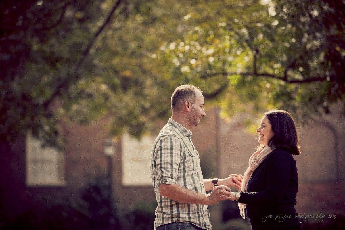 wedding photographers in raleigh nc ~ engagement session for jessica and bo A man and woman holding hands and smiling at each other while standing outdoors. Sunlight filters through the trees in the background, creating a warm and intimate atmosphere.
