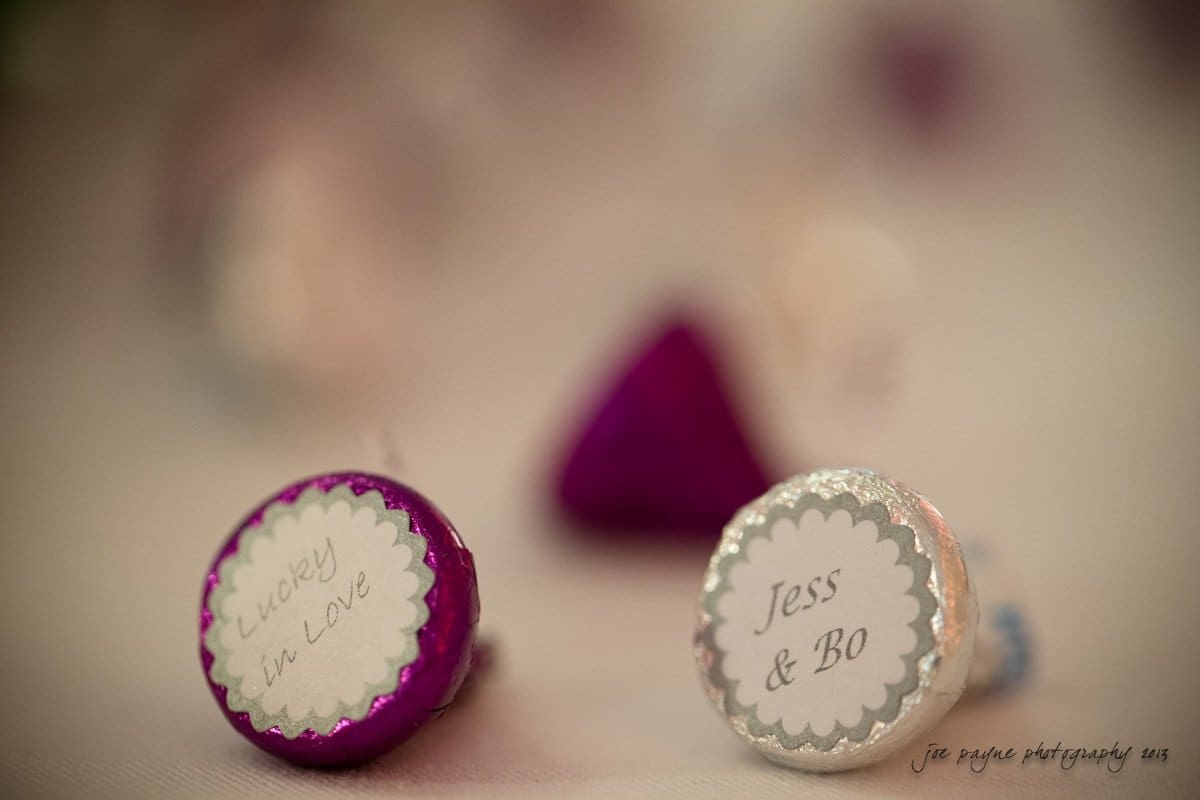 Close-up of chocolate kisses in colorful wrappers with personalized labels. Some labels say Lucky in Love and Jess & Bo. The image focuses on the labels with a blurred background.