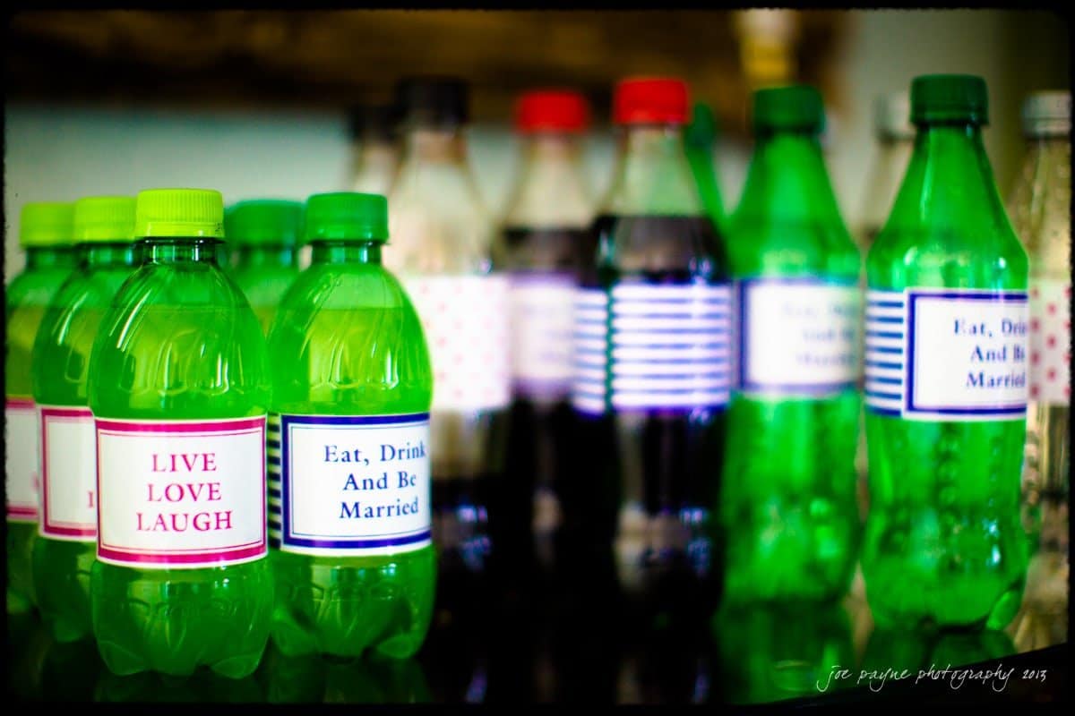 A collection of green and clear plastic bottles with various labels, including LIVE LOVE LAUGH and Eat, Drink And Be Married, displayed on a reflective surface.
