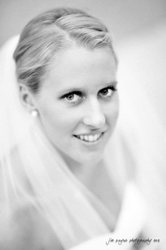 duke chapel weddings ~ bridal session for claire Black and white portrait of a smiling bride with light hair, wearing a veil and pearl earrings, looking up at the camera.