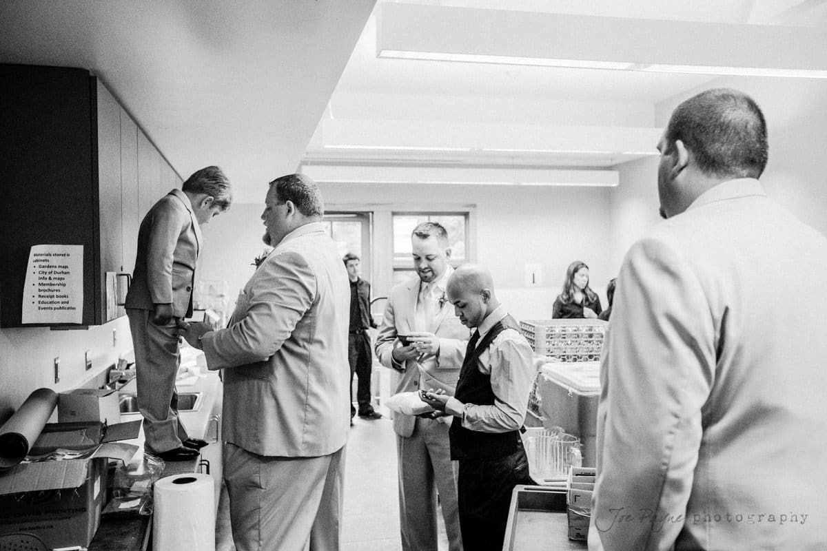 A black and white photo showing several men in suits and a boy in a suit standing on a counter in a kitchen. They are gathered around, some preparing or serving food, with plates and utensils visible on the counter.