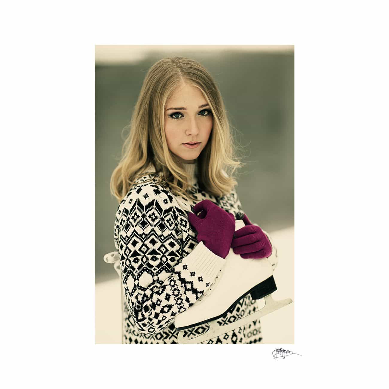 A woman with long blonde hair wearing a patterned sweater and magenta gloves holds ice skates on her shoulder. She stands against a neutral background, looking at the camera with a relaxed expression.