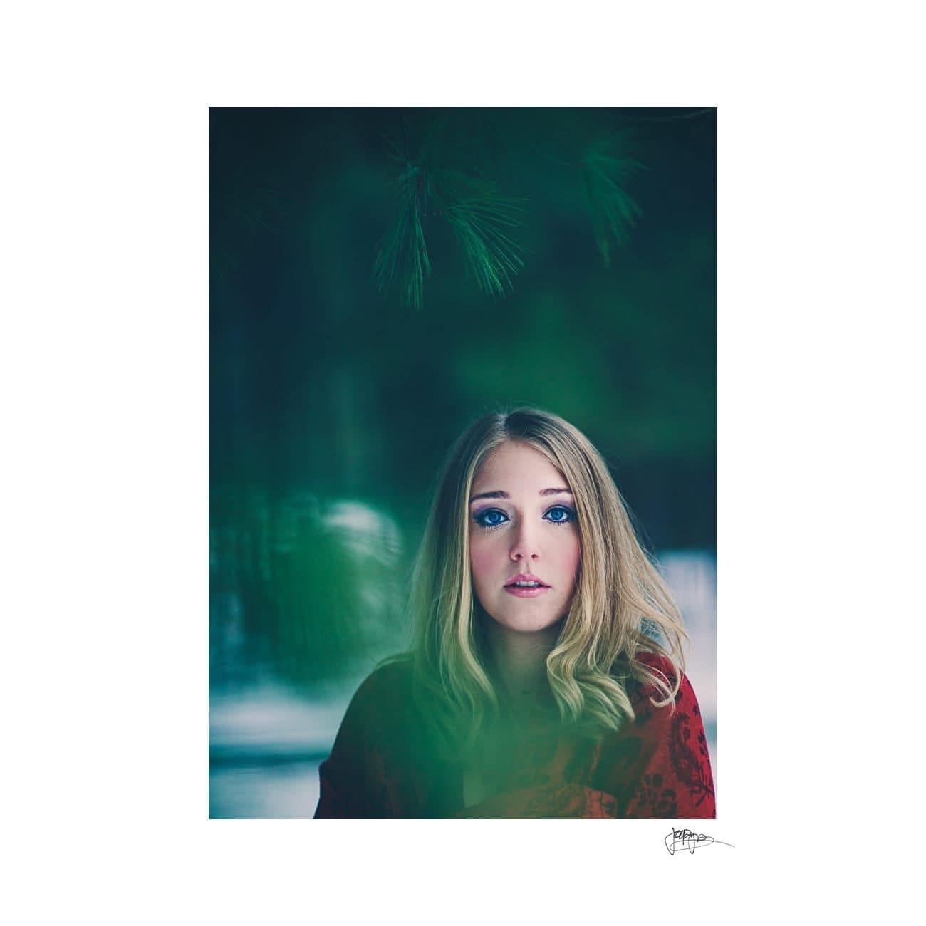 A woman with long blonde hair and blue eyes looks towards the camera with a serene expression. Shes partially obscured by soft, out-of-focus green foliage, creating a dreamy, introspective atmosphere.