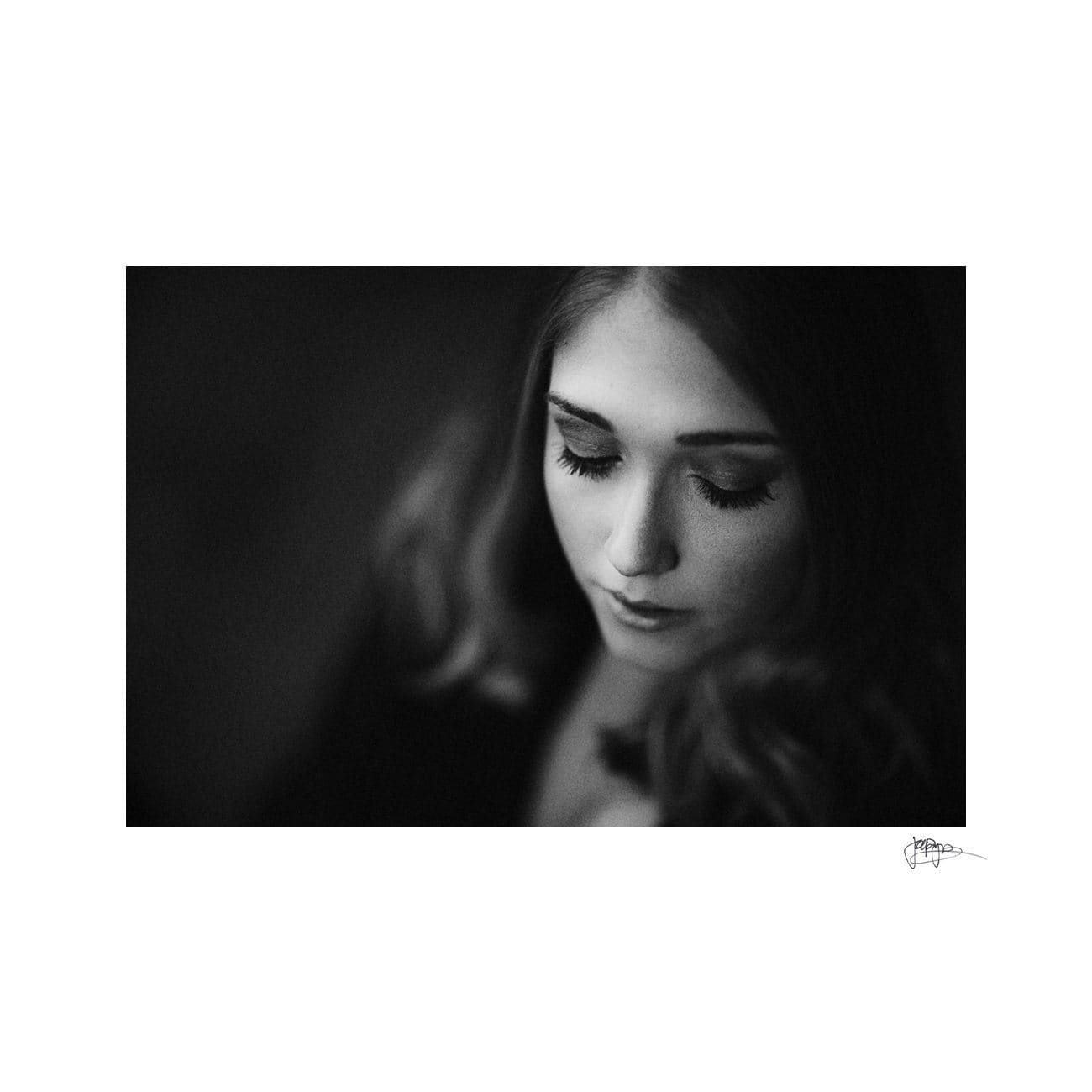 A black and white portrait of a woman with long hair looking down thoughtfully. The image focuses on her serene expression and delicate eyelashes.