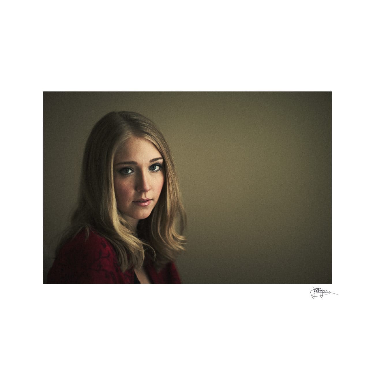 A woman with long, blonde hair and a serious expression gazes softly toward the camera, set against a muted background. She is wearing a red top, and the lighting creates a calm and contemplative atmosphere.