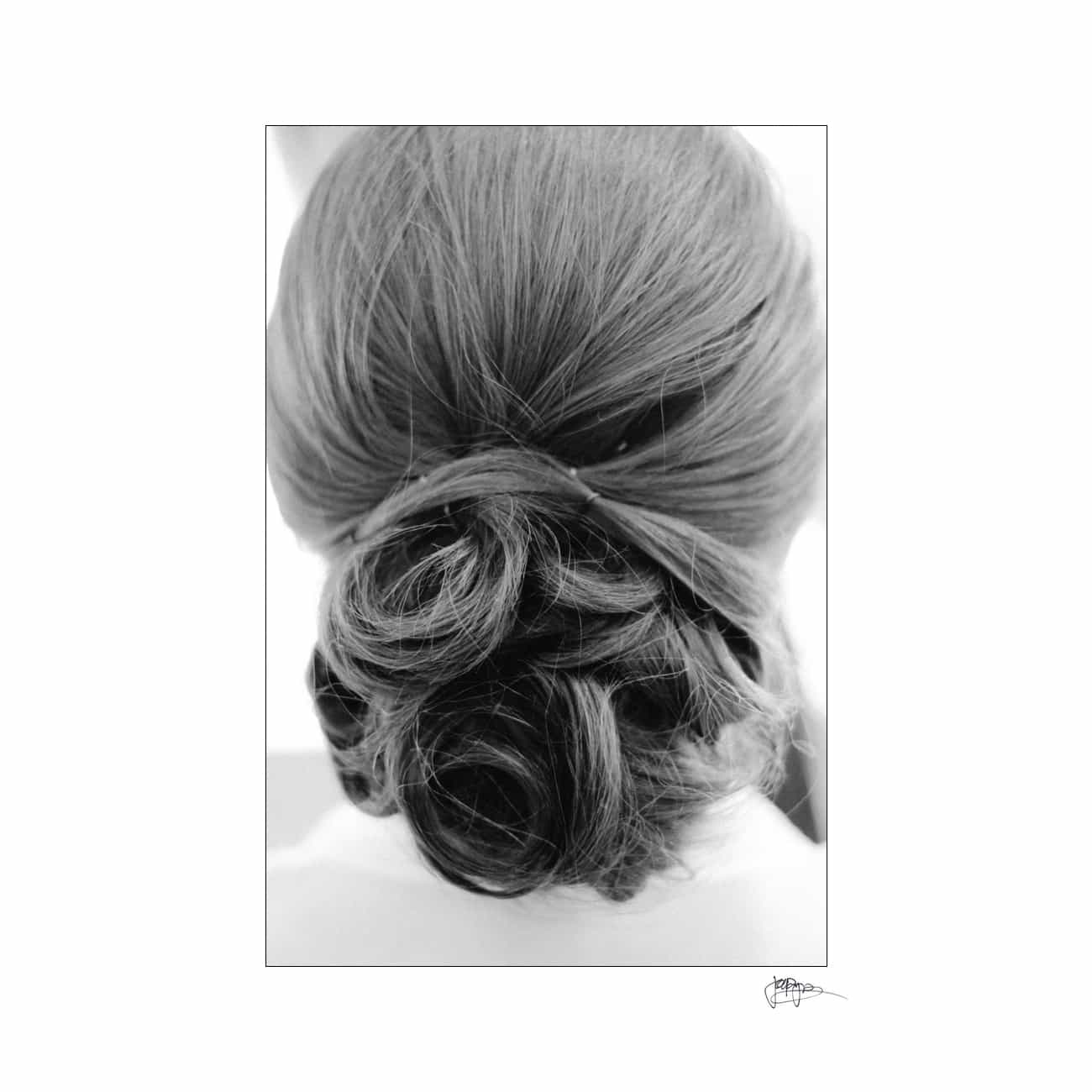Black and white photograph of a person’s intricately styled hair bun from the back, with smooth, swirling sections creating a classic, elegant look.