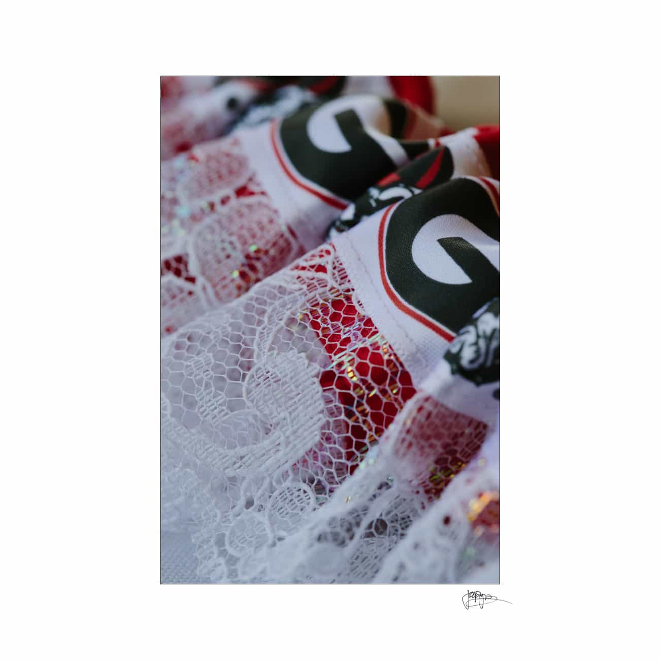 Close-up of a decorative fabric featuring red and white lace details. The fabric includes a bold design with the letter G in black on a white background.