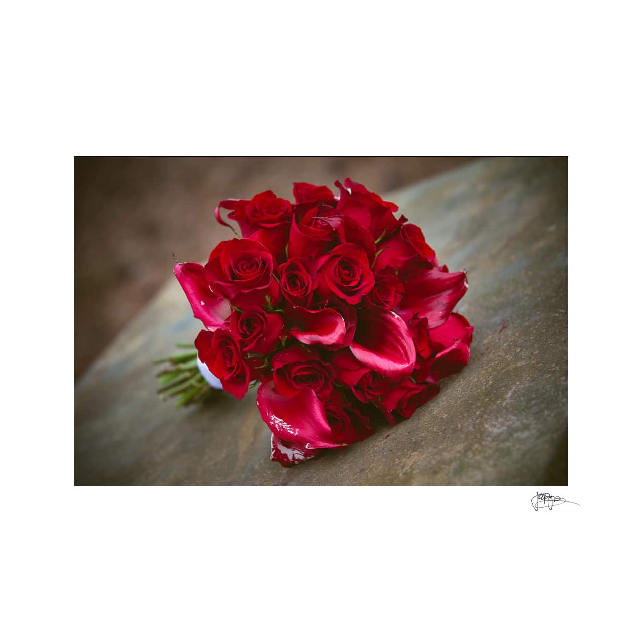 A bouquet of red roses and pink lilies rests on a stone surface. The flowers vibrant colors contrast with the muted background, creating a striking and elegant composition.