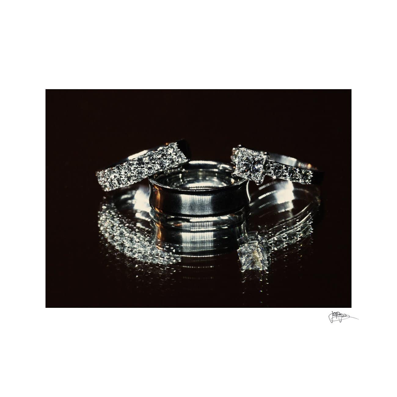 Three silver rings, including two with diamond settings and a plain band, are arranged artistically on a reflective dark surface, creating a mirrored effect. The diamonds sparkle, adding an elegant touch to the composition.