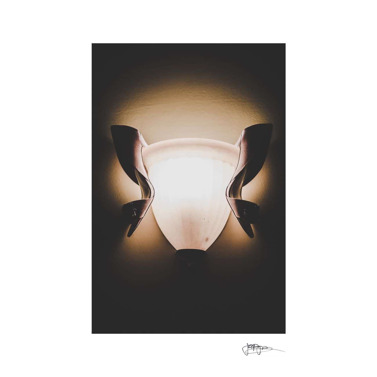 A wall-mounted light fixture is illuminated against a dark background. The light has a frosted glass shade with an organic shape, creating a soft glow and a symmetrical appearance.