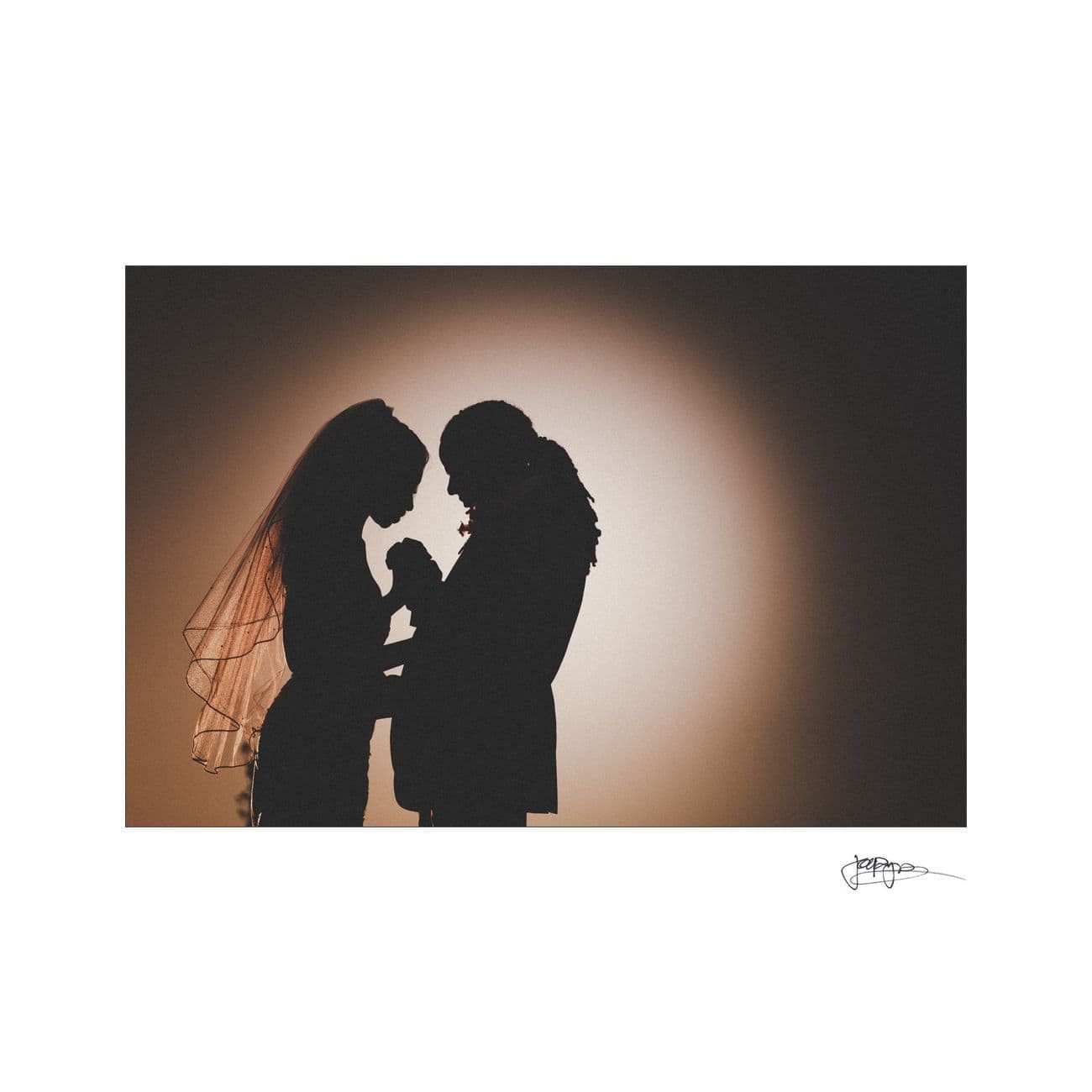 Silhouette of a couple facing each other, holding hands. The bride wears a veil and the groom has long hair. They stand against a bright, circular backdrop, creating a romantic and intimate scene.
