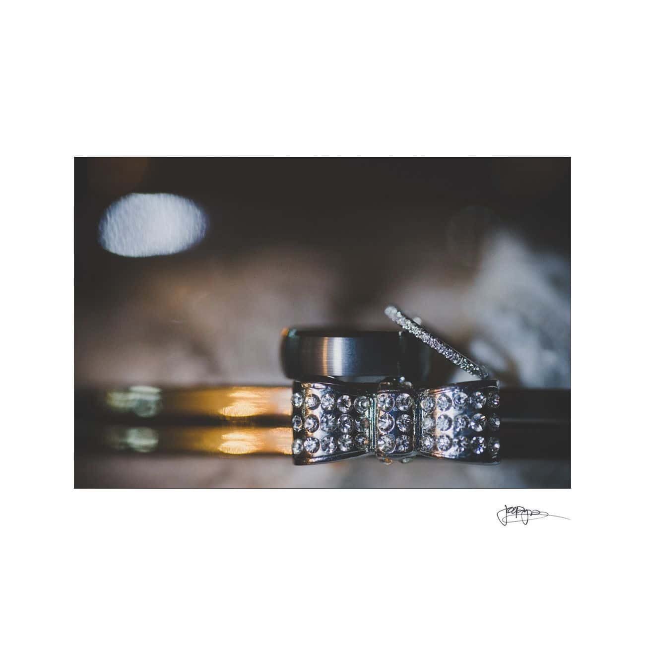 Close-up of a collection of rings, including a gold band, a silver ring with a gemstone, and a diamond-studded bow-shaped piece. The image captures the intricate details and sparkle of the jewels against a soft-focus background.