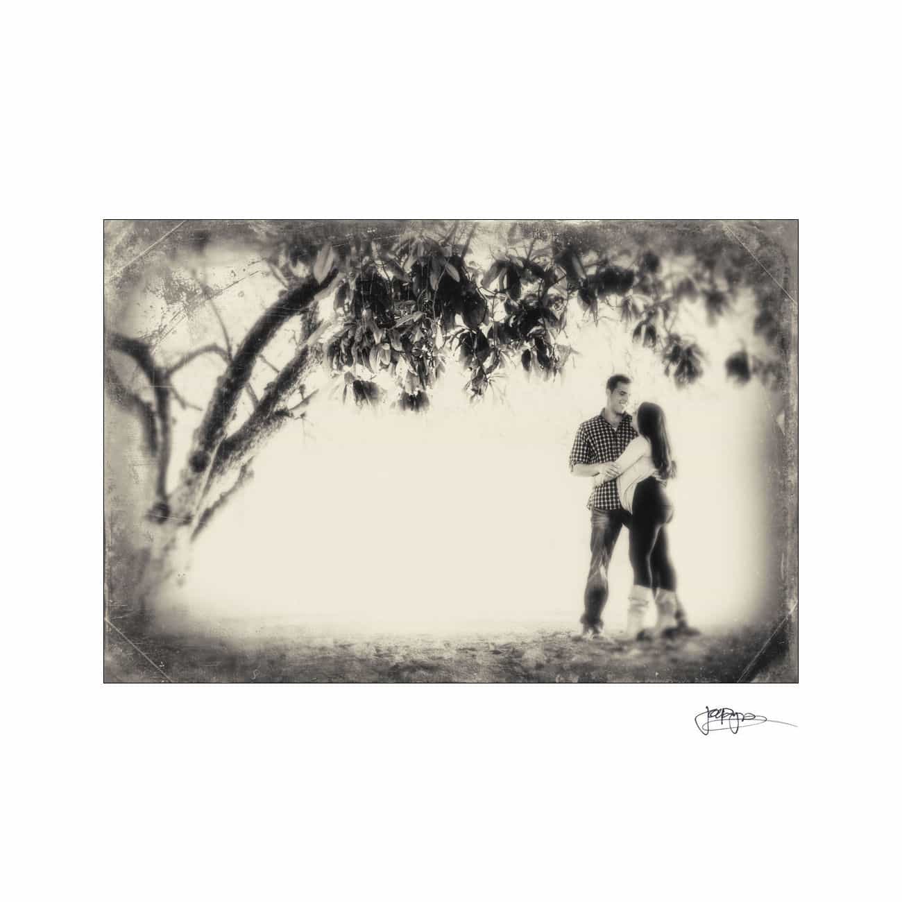 A sepia-toned image of a couple standing under a tree, facing each other. The scene has a soft, vintage feel with blurred edges, creating a dreamy atmosphere.
