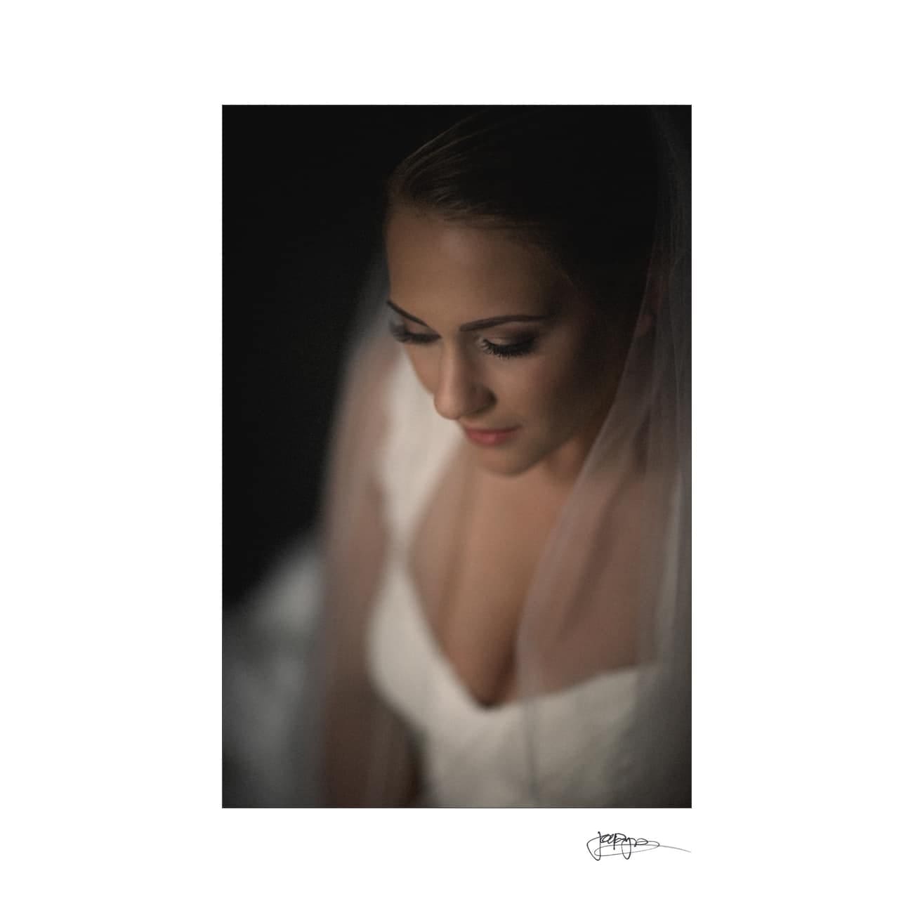A serene bride in a white dress, captured in soft lighting with her eyes closed and head gently tilted. A veil surrounds her, creating an intimate and peaceful atmosphere.