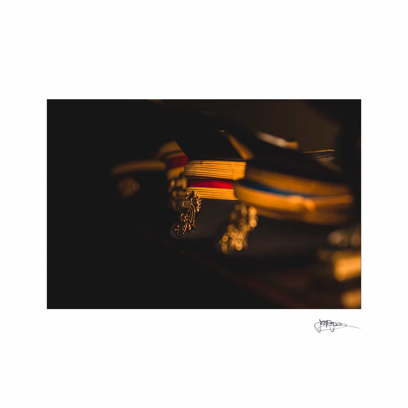 chapel hill wedding photographer - alexandra & john Close-up of military caps with shiny gold insignias and colorful bands, including red and blue. The dark background contrasts with the illuminated details of the caps, creating a dramatic effect.