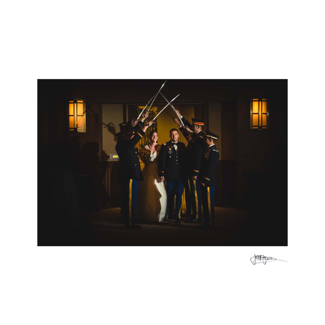 chapel hill wedding photographer - alexandra & john A bride and groom walk under a traditional military saber arch formed by uniformed soldiers inside a dimly lit room. The couple looks happy, surrounded by the warm glow of wall lamps.