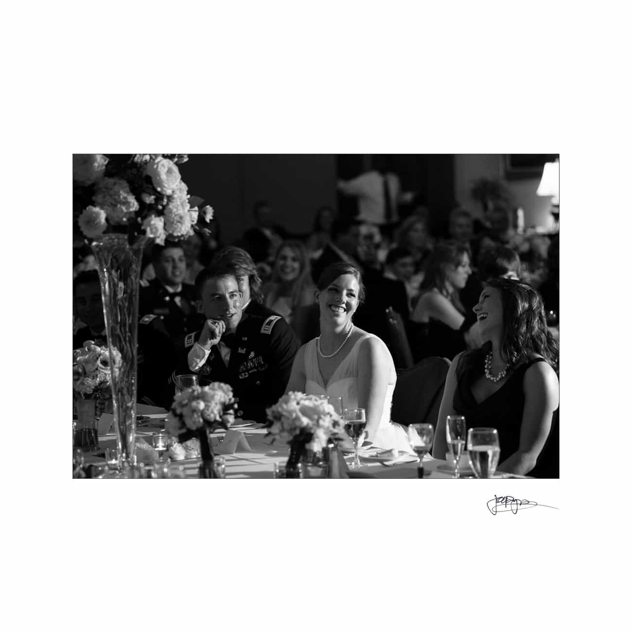 chapel hill wedding photographer - alexandra & john A black and white photo of people seated at a formal event, laughing and enjoying themselves. The table is adorned with flowers and glassware. The atmosphere appears lively and celebratory.