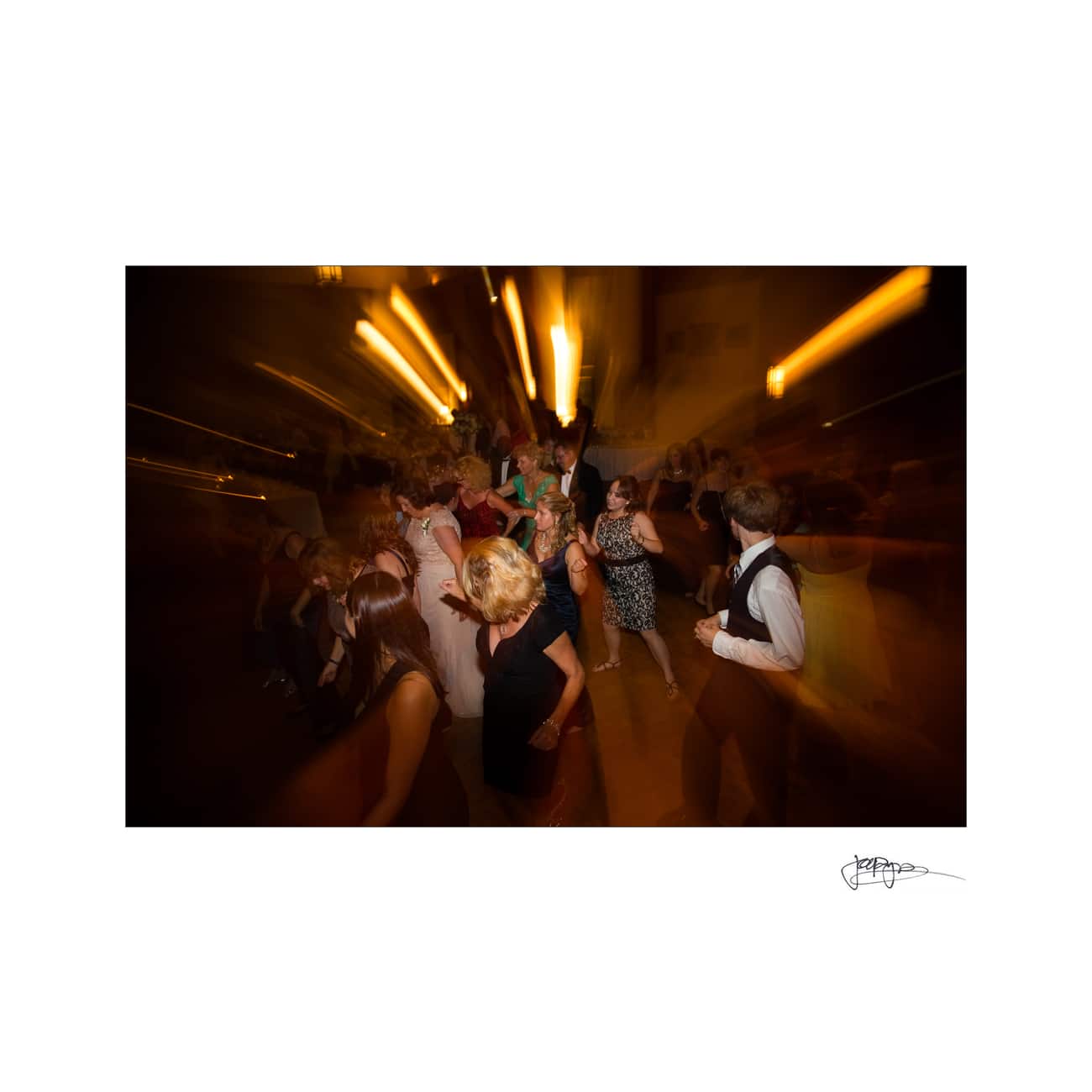 chapel hill wedding photographer - alexandra & john A group of people dancing energetically at a party, captured with a motion blur effect. The warm lighting creates a dynamic and lively atmosphere.