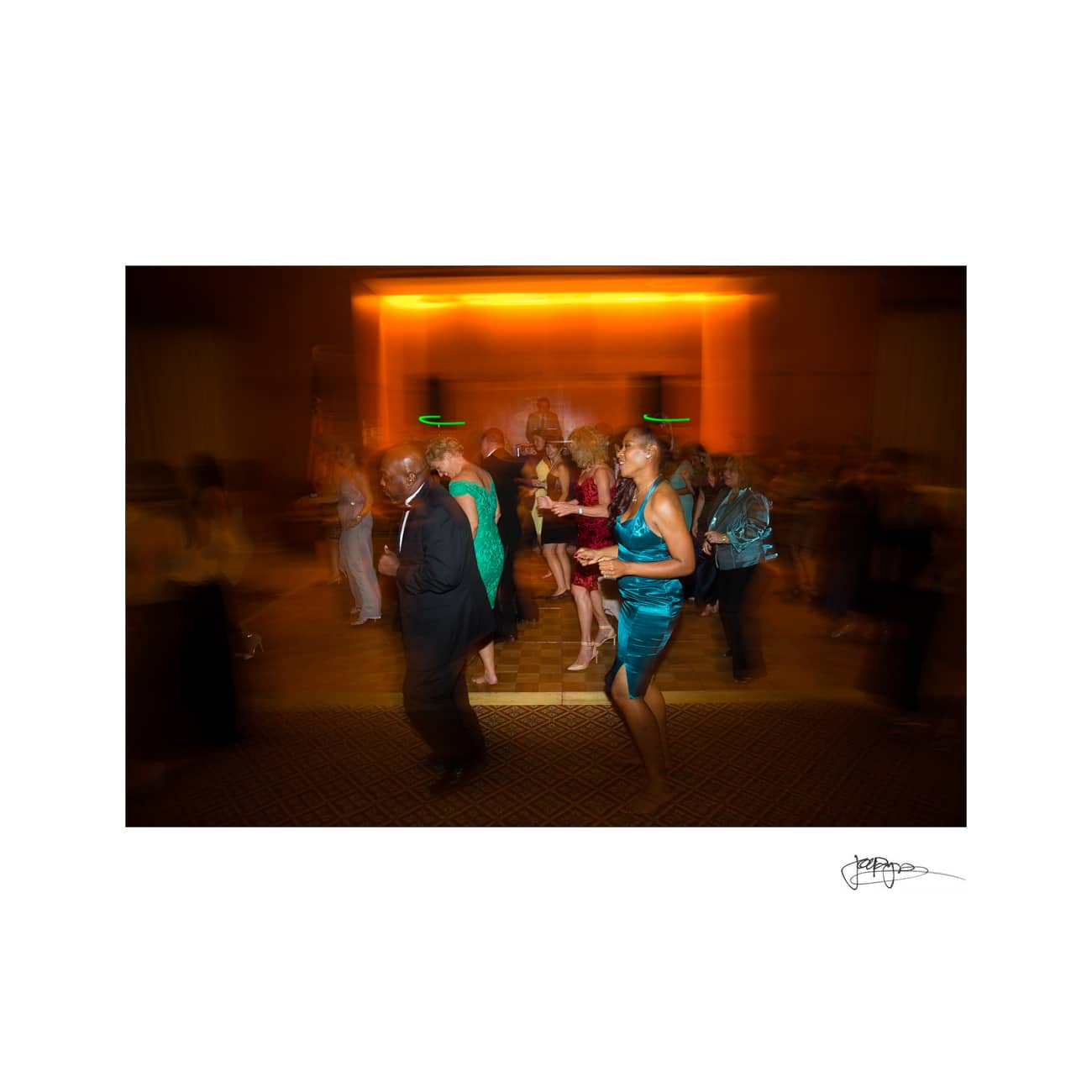 chapel hill wedding photographer - alexandra & john A group of people dancing in a dimly lit room. The photo has a motion blur effect, creating a sense of movement. The room has warm lighting, and the people are dressed in formal or semi-formal attire.