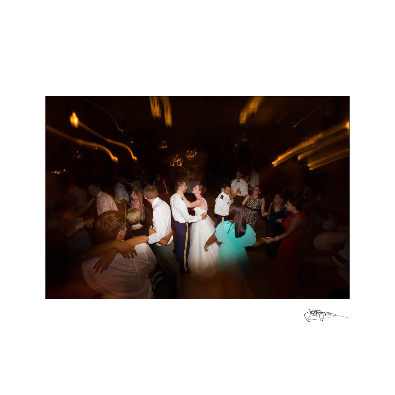 chapel hill wedding photographer - alexandra & john A bride and groom embrace and dance in the center of a dimly lit room, surrounded by guests in a lively atmosphere. The lighting creates a blurred effect, adding a sense of movement and energy to the scene.
