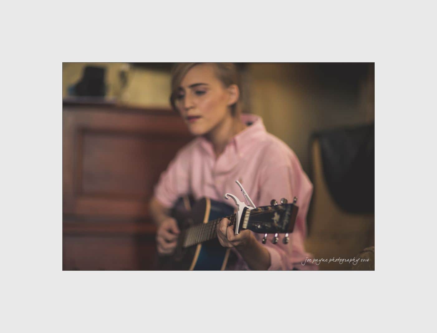 wilmington wedding photographer - nichole & eric A person in a pink shirt plays an acoustic guitar indoors. The background is softly blurred, suggesting a cozy setting. The focus is on the instrument and the persons expression, conveying a relaxed, introspective mood.
