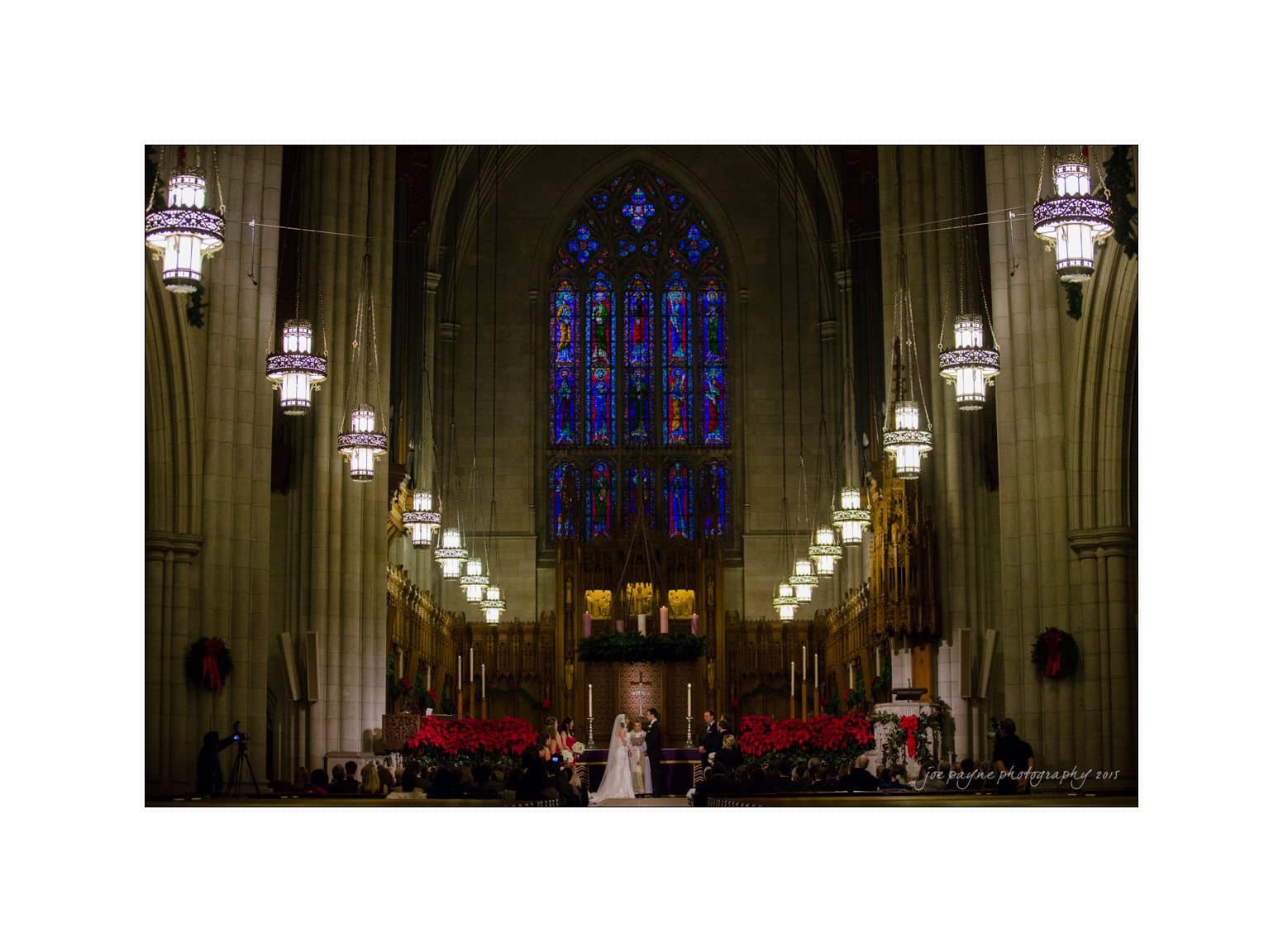 A couple stands at the altar of a grand cathedral during their wedding ceremony. The interior features tall arches, stained glass windows, and hanging chandeliers, creating a majestic and solemn atmosphere.