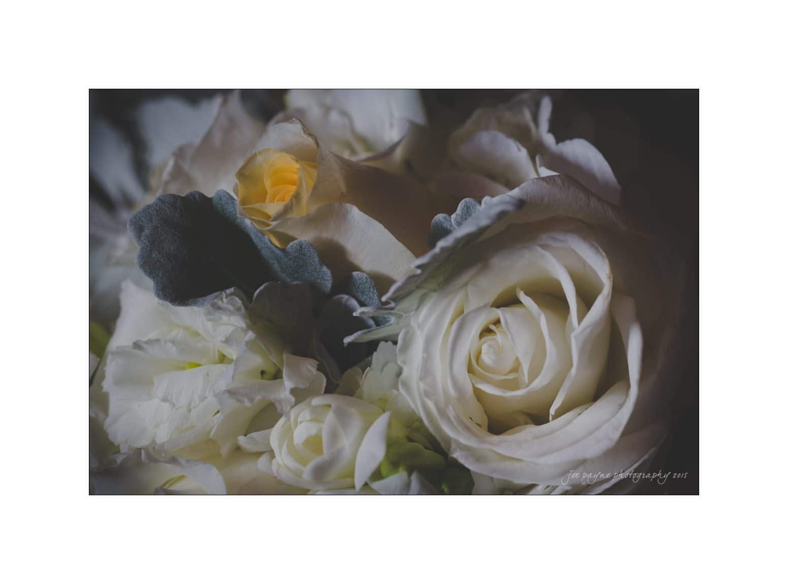 Close-up of a bouquet featuring white roses and cream-colored flowers surrounded by soft, gray-green leaves. The petals are delicately unfurled, highlighting their intricate textures and gentle hues.