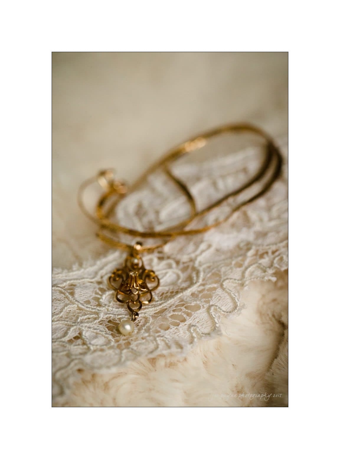 A gold bangle with an intricate pendant and pearl is elegantly placed on a piece of white lace fabric. The background is soft and blurred, highlighting the jewelrys delicate design.