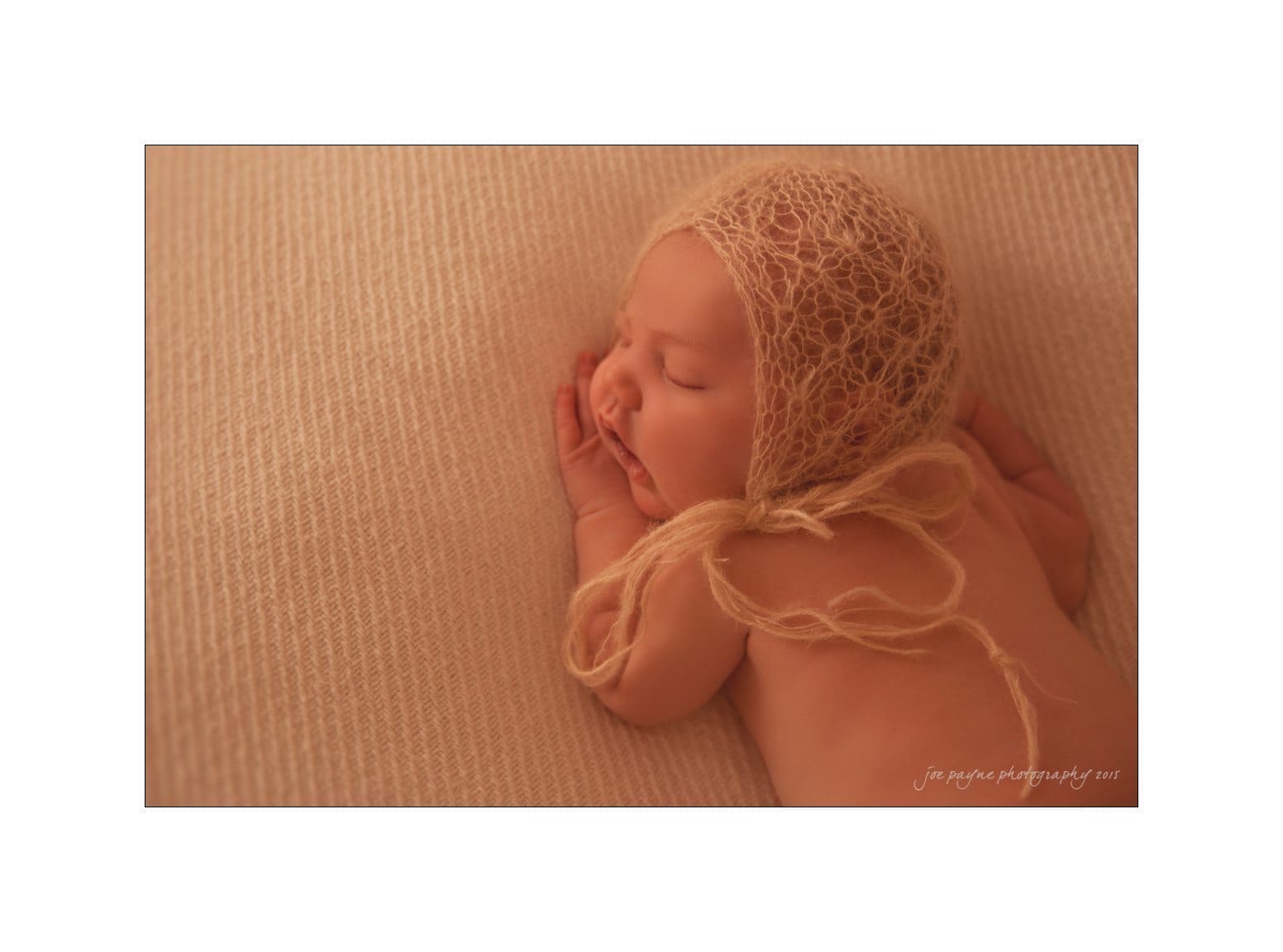 raleigh newborn photographer - baby patton A baby sleeps peacefully on a textured beige blanket, wearing a delicate knitted bonnet. The setting is warm and soft, emphasizing the serene atmosphere.