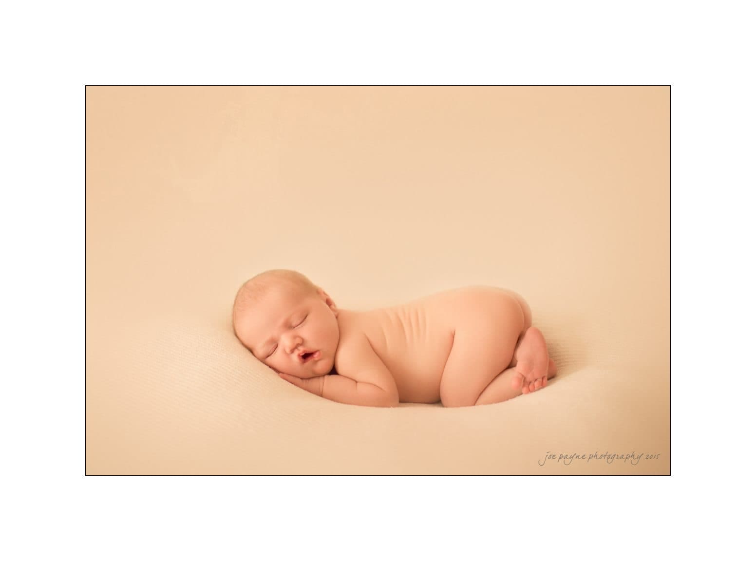raleigh newborn photographer - baby patton A newborn baby sleeps peacefully on a soft, cream-colored blanket. The baby is curled up on their side with hands tucked under their cheek. The background is simple and minimal, enhancing the serene and gentle atmosphere.