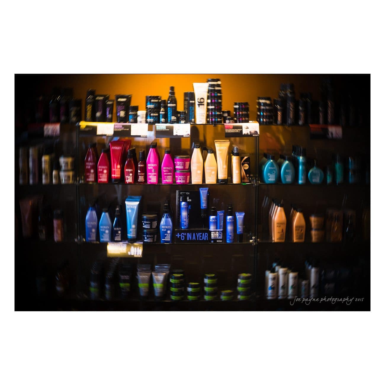 Shelves filled with various colorful bottles and containers of hair care products, including shampoos and conditioners, displayed in a dimly lit setting.