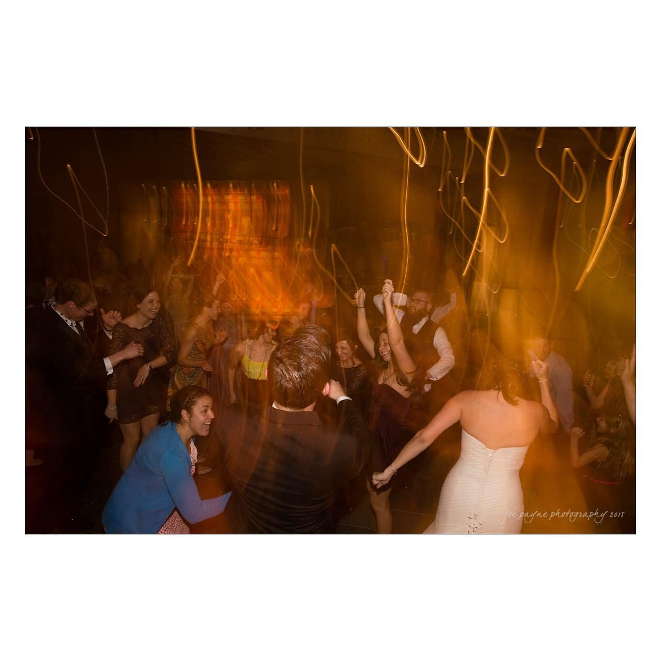 A lively wedding reception with guests dancing energetically on the dance floor. Motion blur and colorful lighting convey excitement and movement as people celebrate together.