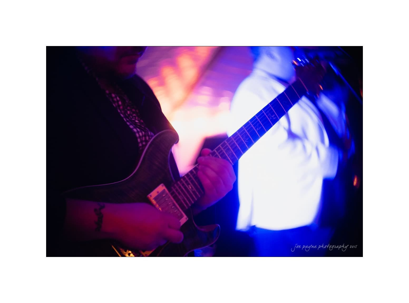 NC wedding photography - rachel & joe A musician playing an electric guitar on stage, with a blurred, colorful background of purple and blue lights. The scene captures the dynamic atmosphere of a live performance.