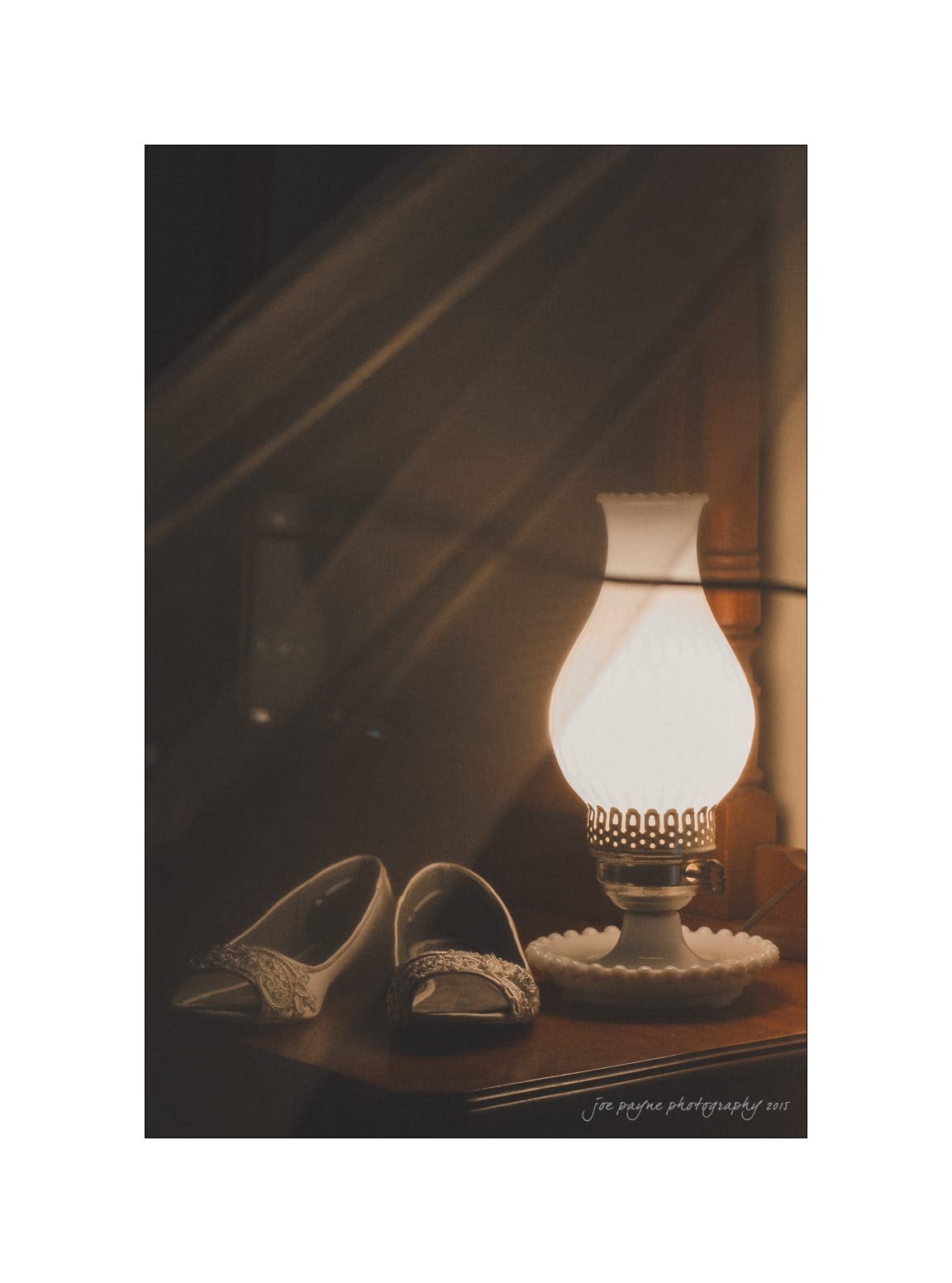 NC wedding photography - rachel & joe A pair of elegant shoes sits beside a vintage-style lamp casting a warm glow on a wooden surface. The scene exudes a nostalgic and cozy atmosphere.