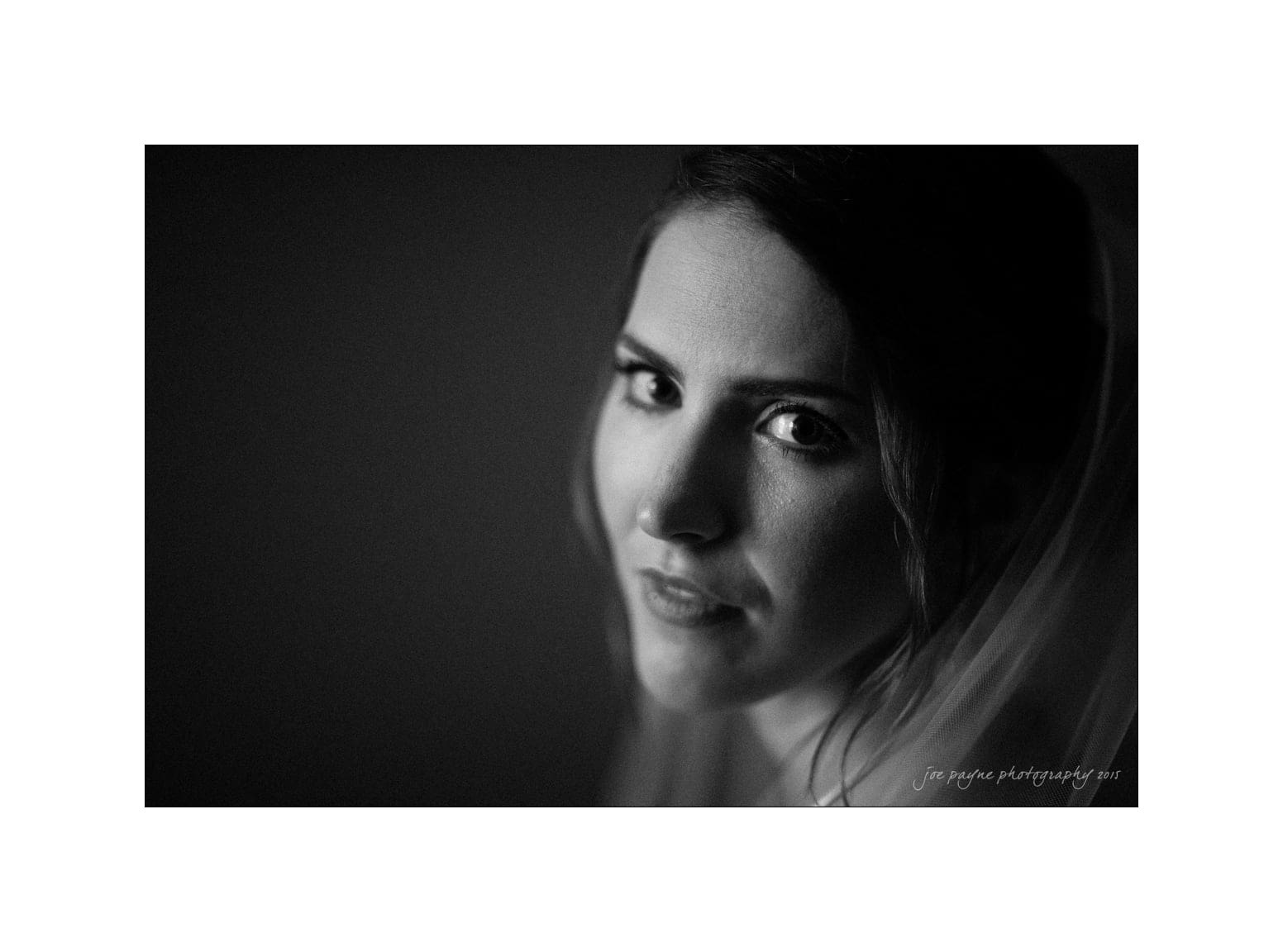 NC wedding photography - rachel & joe Black and white portrait of a woman with a soft gaze, partially illuminated from the side, against a dark background. She has a slight smile and her hair is styled back, with some loose strands framing her face.