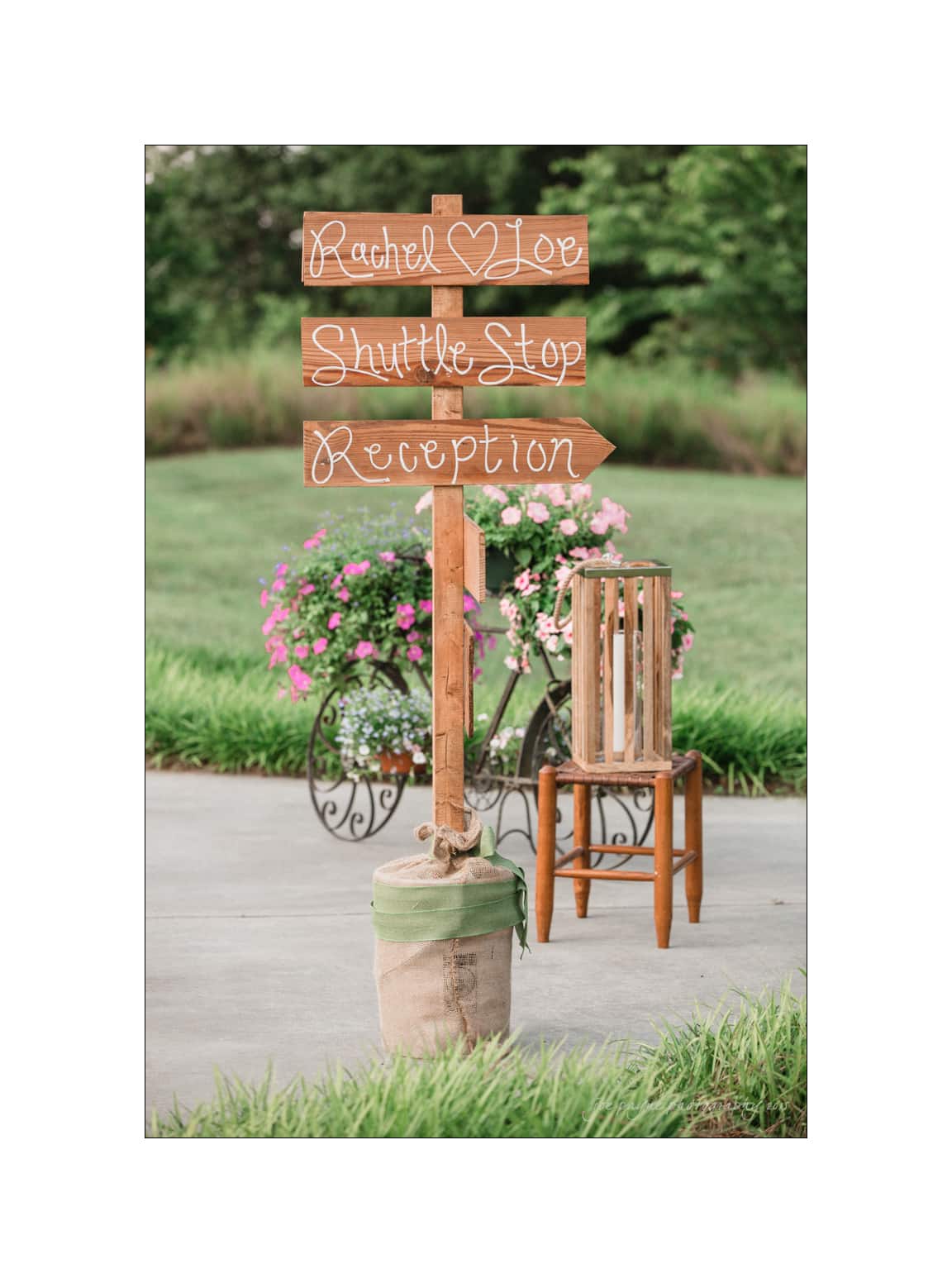 NC wedding photography - rachel & joe A wooden signpost with handwritten text reading Rachel ? Joe, Shuttle Stop, and Reception stands on a patio. Its decorated with a pink flower pot, next to a wooden chair, with greenery in the background.
