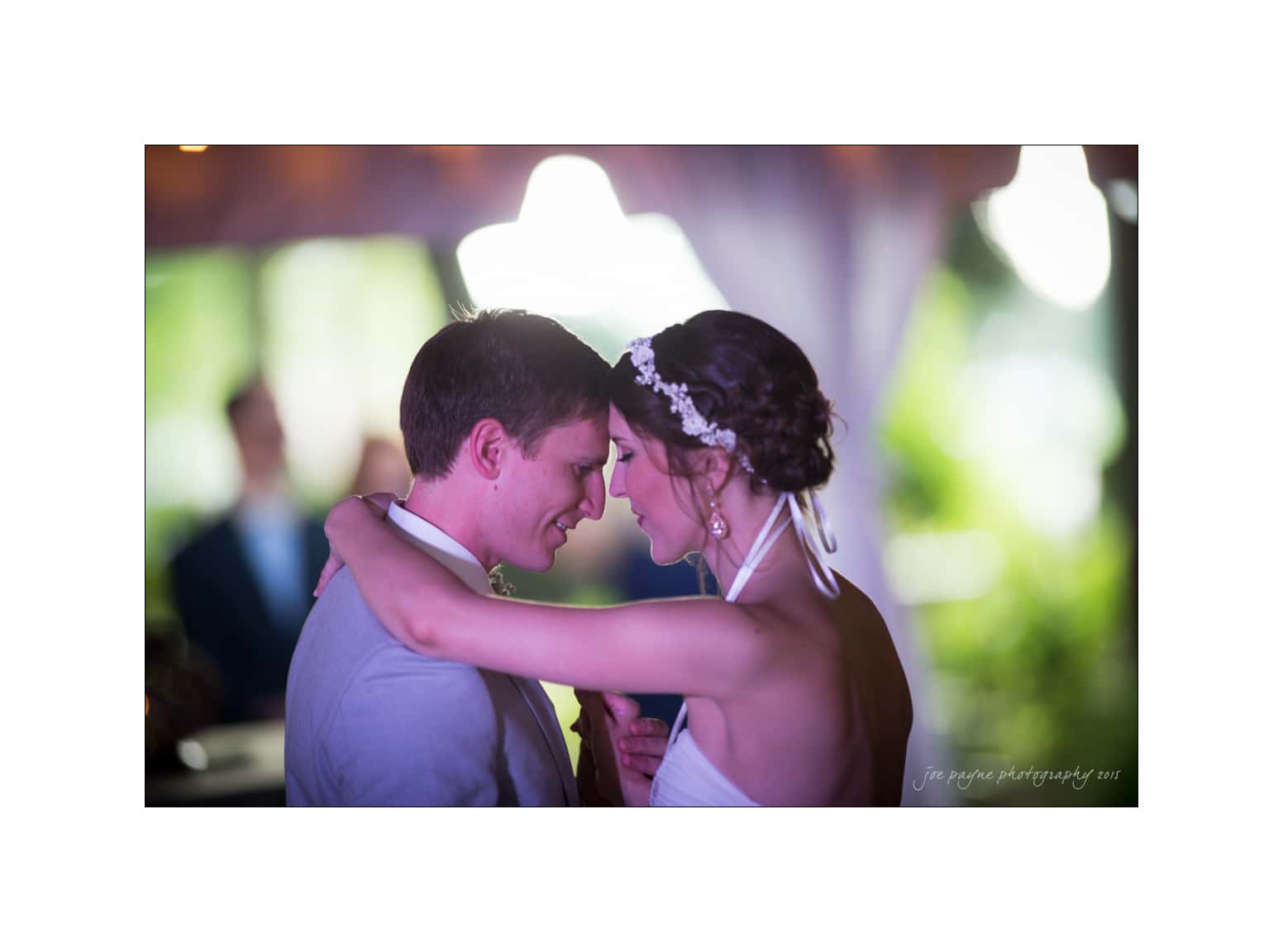 NC wedding photography - rachel & joe A bride and groom share a joyful embrace during their wedding dance. The bride wears a strapless dress and headband, while the groom is in a light-colored suit. The background is softly blurred, creating a romantic atmosphere.