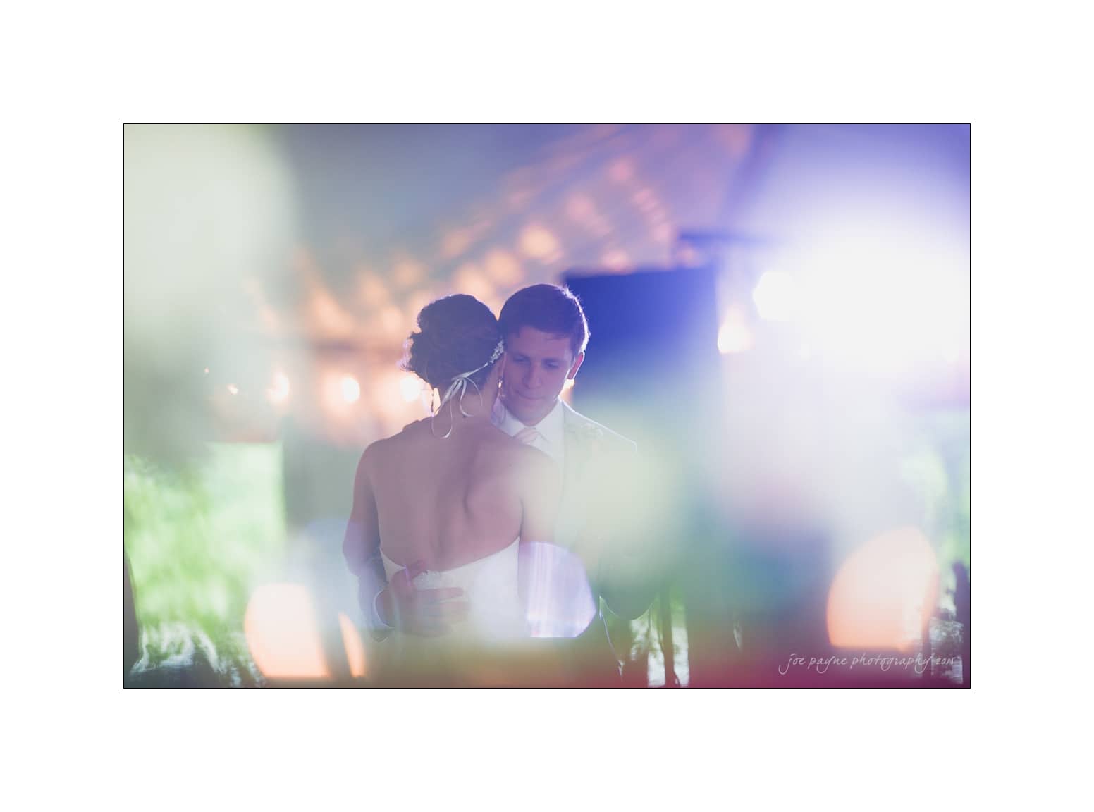 NC wedding photography - rachel & joe A couple shares a quiet embrace at their wedding, standing closely together under soft, dreamy lighting. The image has a gentle, romantic glow with blurred foreground elements enhancing the intimate atmosphere.