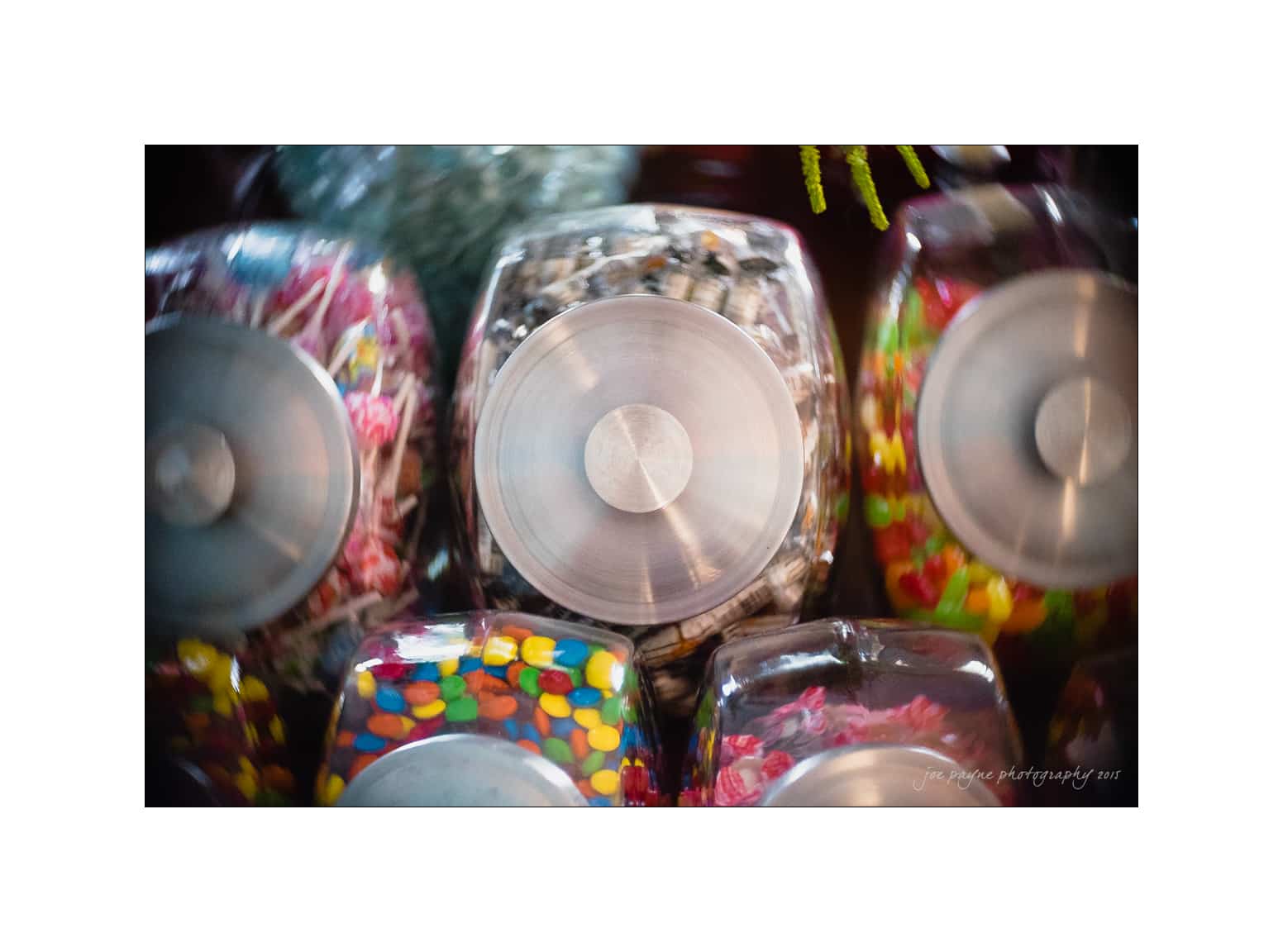NC wedding photography - rachel & joe A collection of glass jars filled with various colorful candies, including jelly beans and other sweets, viewed from above. The jars have round metal lids, creating a vibrant display.