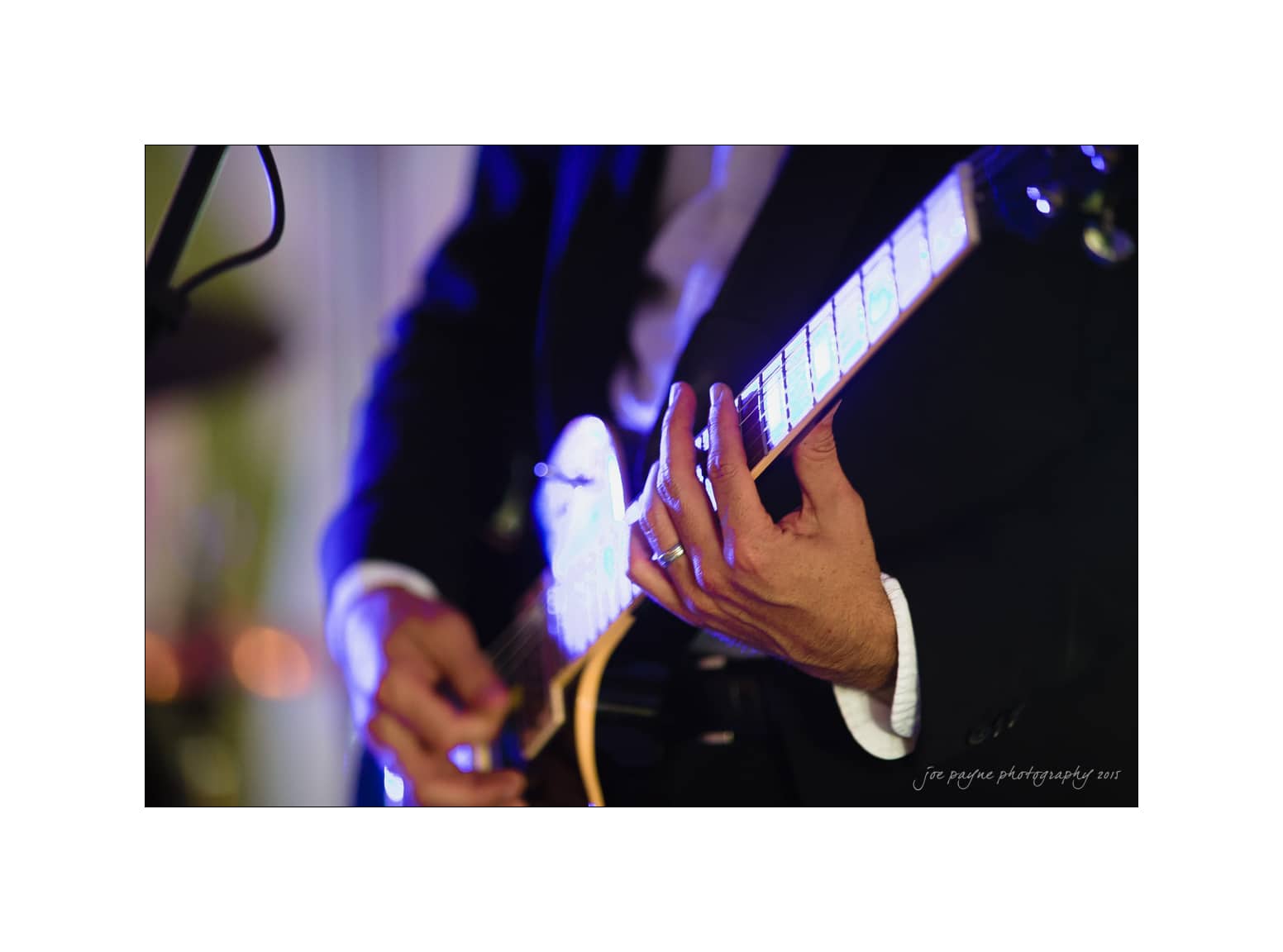 NC wedding photography - rachel & joe Close-up of a person in formal attire playing an electric guitar. The focus is on their hands and the guitar, with blurred background lights creating a warm ambiance.