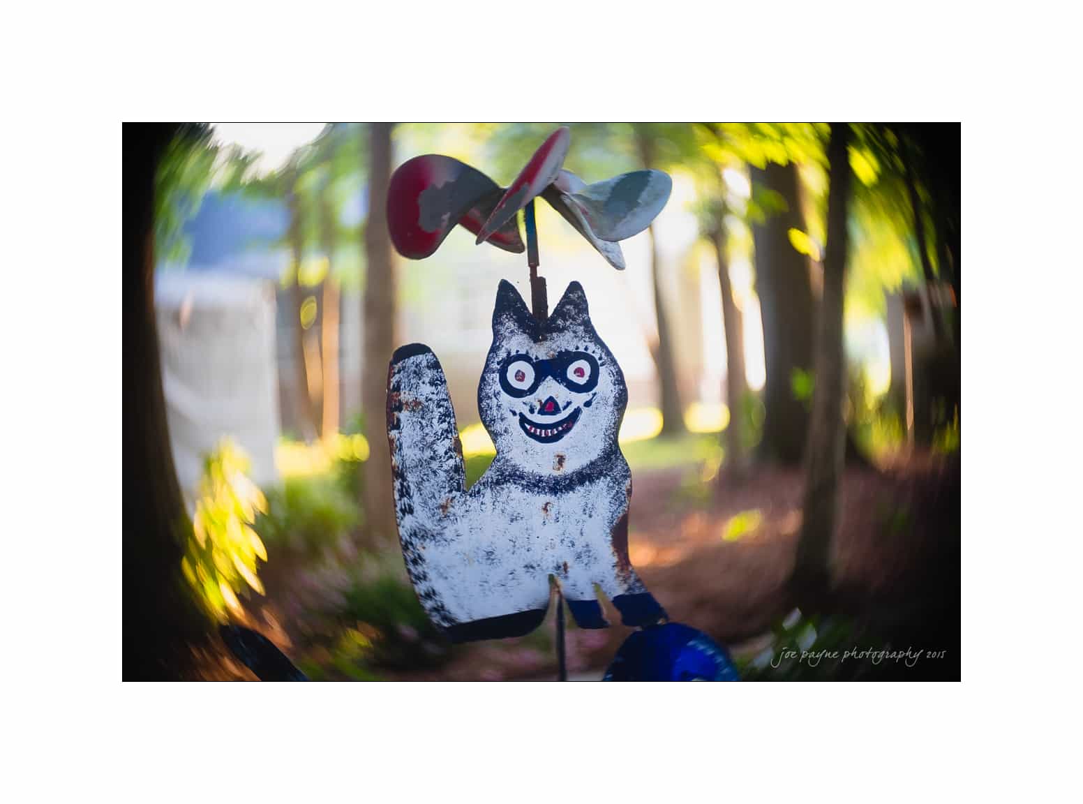 NC wedding photography - rachel & joe A whimsical cat-shaped garden ornament with a wide smile and big eyes spins in a sunlit garden. The background is softly blurred with trees and foliage.