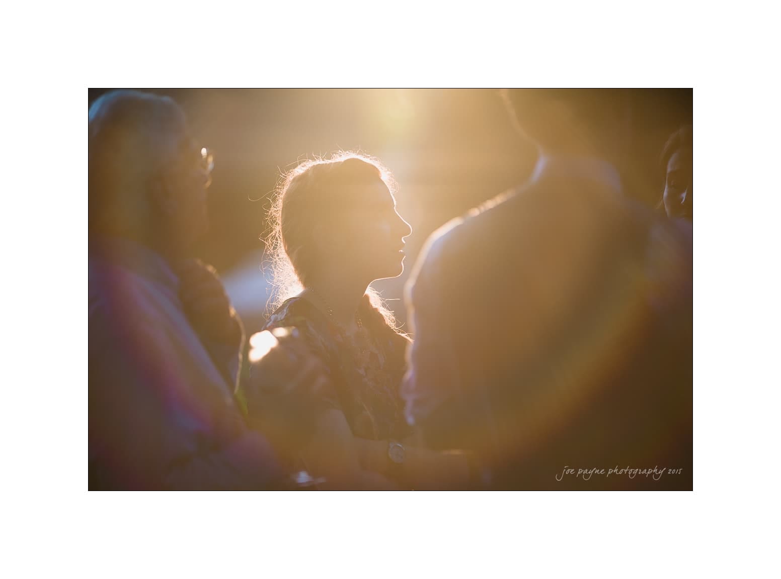 NC wedding photography - rachel & joe A group of people standing together with a warm, glowing light illuminating them from behind. The light creates a soft silhouette around the central figure, capturing a moment of conversation or interaction.