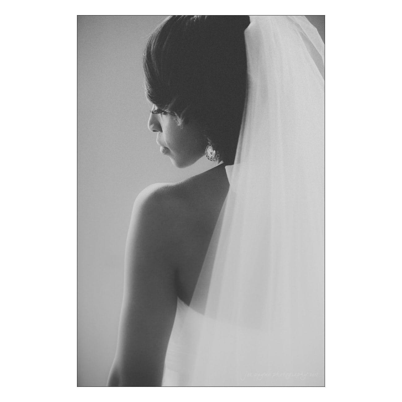 Black and white portrait of a bride from the side, showcasing her veil and elegant hairstyle. The image has a soft, timeless feel.