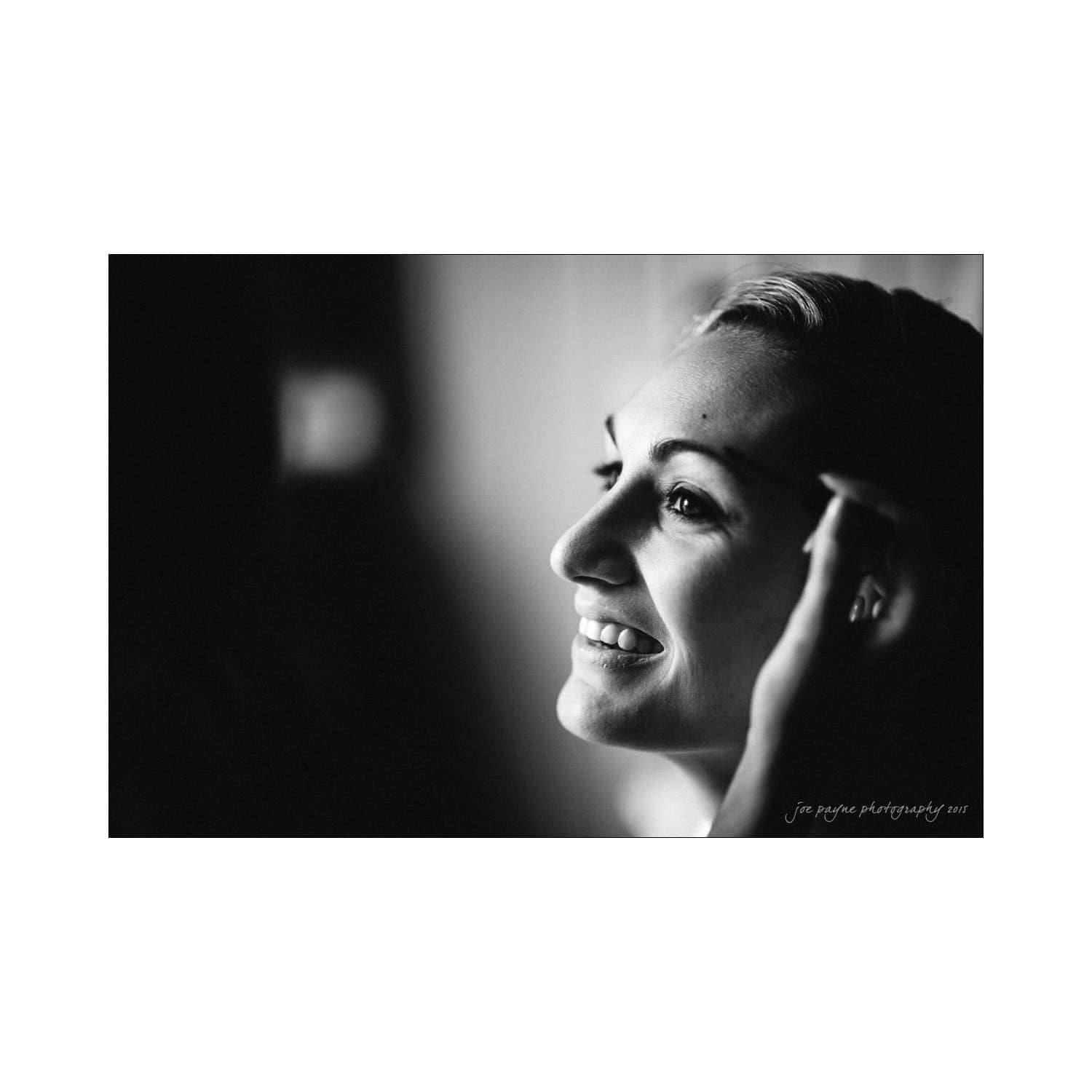 chapel hill wedding photography - nicole & wayne Black and white image of a smiling woman in profile, looking towards the light. She holds her hand near her face, exuding a sense of calm and joy.