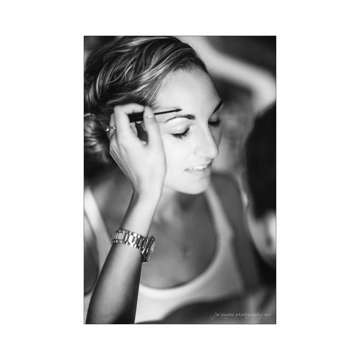 chapel hill wedding photography - nicole & wayne A woman with closed eyes getting her eyebrows groomed, wearing a tank top and a watch, in a black and white portrait.