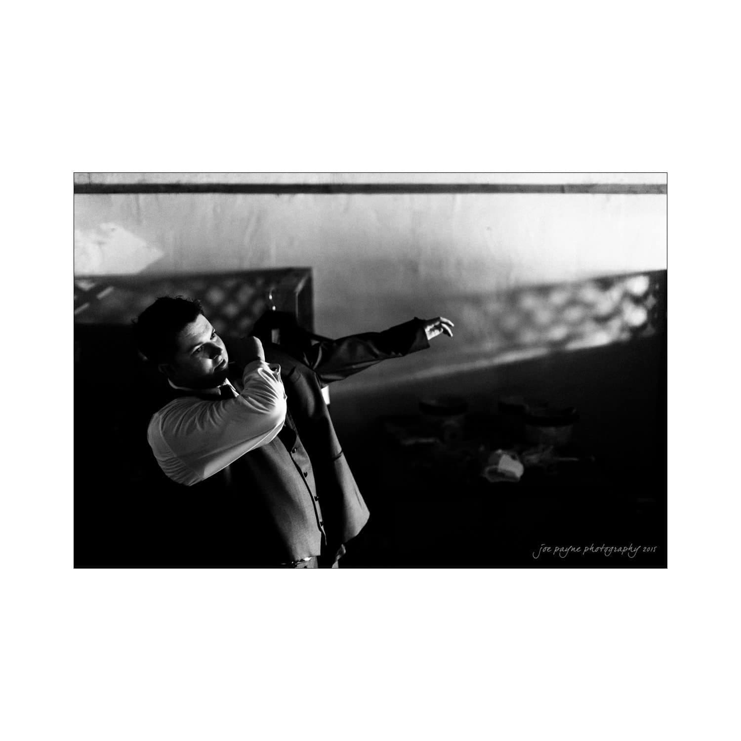 chapel hill wedding photography - nicole & wayne A man in a suit passionately sings or speaks into a microphone, his other arm extended. The setting is dramatic, with contrasting light and shadows on the wall behind him.
