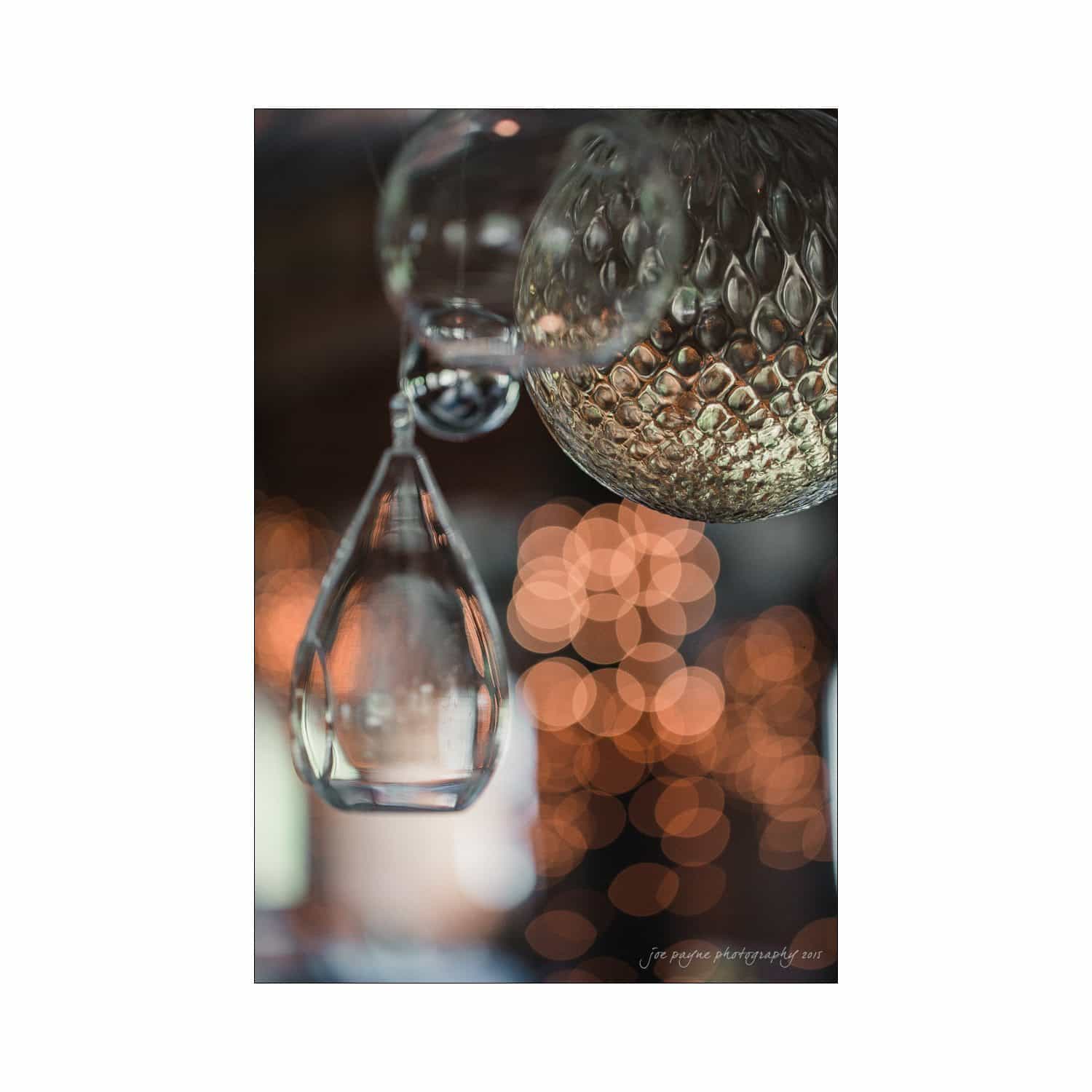 chapel hill wedding photography - nicole & wayne Close-up of decorative hanging glass orbs and drops with textured surfaces, set against a softly blurred background of warm bokeh lights. The image captures a cozy, ambient atmosphere.