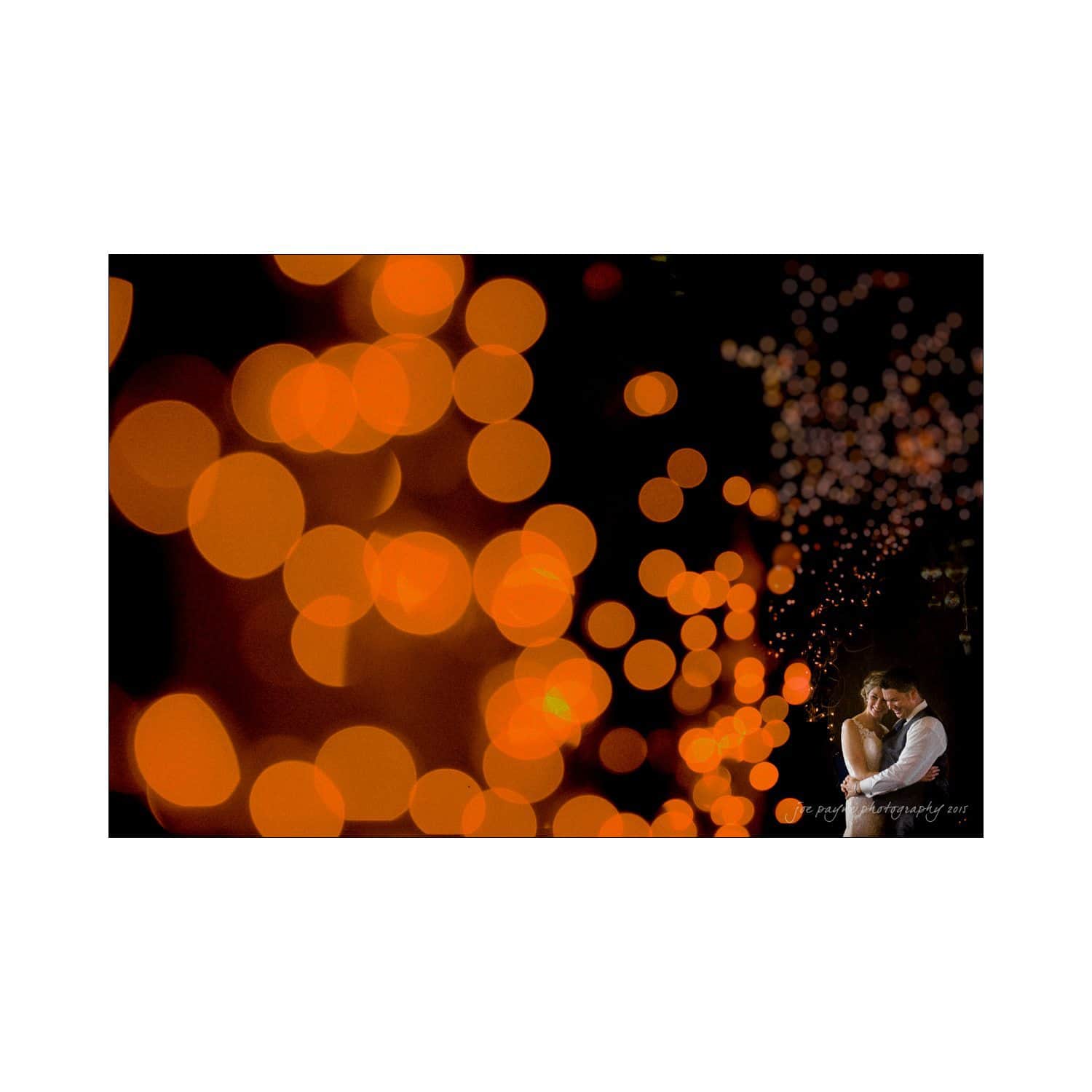 chapel hill wedding photography - nicole & wayne A couple embraces in the corner of a darkened scene, surrounded by glowing orange bokeh lights, creating a dreamy and romantic atmosphere.